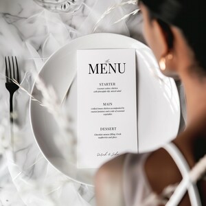 May include: A white menu card with black text, listing the starter, main, and dessert options for a wedding reception. The menu includes coconut cashew chicken, grilled lemon chicken, and chocolate mousse. The card is signed "Sarah & John".