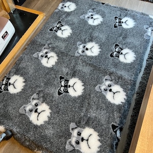 May include: A rectangular grey fuzzy blanket featuring a repeating pattern of white and grey dog faces with black ears and black eye patches. The plush fabric has a soft, textured appearance, and the dog faces are evenly distributed across the surface.