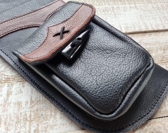 Könnte beinhalten: Eine schwarze Ledertasche mit einer braunen Lederklappe und einem Metallverschluss. Die Tasche hat ein gesticktes X auf der Klappe.