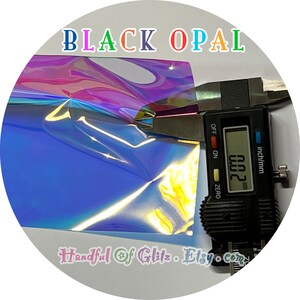 Holographic, iridescent foil set, showing iridescence, sheen  and thickness for Black Opal mylar during a caliper measurement. Individual sheet or set of 3.