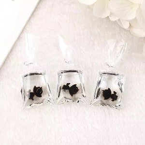 May include: Three clear plastic bags with black butterfly charms inside. The bags are hanging from a white surface.