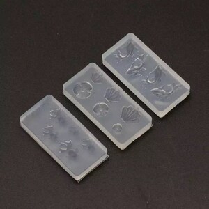 May include: Three clear silicone molds for crafting. The molds feature different designs: one with seashells, one with flowers, and one with fish.