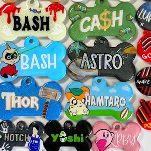 Op de afbeelding: Een verzameling van 10 kleurrijke, botvormige hondenpenningen met verschillende namen en ontwerpen. De penningen zijn gemaakt van een glinsterend materiaal en hebben namen zoals "Bash", "Cash", "Astro", "Thor", "Hamtaro", "Yoshi" en "Kirby".