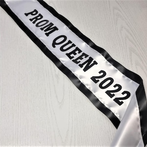 May include: White satin sash with black trim and the text "Prom Queen 2022" in black.