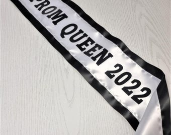 May include: White satin sash with black trim and the text "Prom Queen 2022" in black.