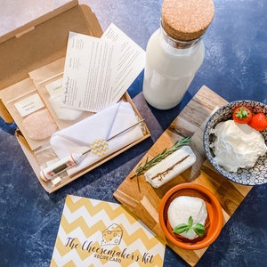 May include: A cheese-making kit with ingredients, instructions, and a recipe card. Includes a bottle of milk, a wooden cutting board with cheese, a bowl of fresh cheese with strawberries, and a small bowl of cheese with basil.