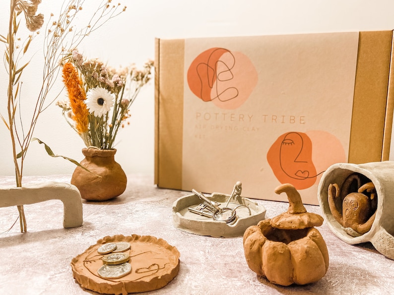 May include: A Pottery Tribe air-drying clay kit with handmade clay objects. The objects include a vase with dried flowers, a pumpkin-shaped container, a tray with coins, a small dish with keys, and a decorative sculpture.
