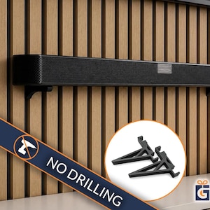 Könnte beinhalten: Eine schwarze Soundbar, die mit zwei schwarzen L-förmigen Halterungen an einer Wand befestigt ist. Ein kreisförmiger Einsatz zeigt die beiden schwarzen Kunststoffhalterungen separat. Ein blaues Banner zeigt den Text NO DRILLING mit einem Bohrer-Symbol.