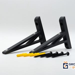 May include: Two matte black metal shelf brackets with a triangular support structure, each featuring two mounting holes on the vertical back plate. Included are four black screws and four yellow plastic wall anchors for installation.