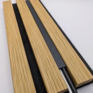 May include: A wooden desk tidy featuring three light-coloured wooden slats and a black felt base. A black metal strip and a black and white cable are visible. The organiser is designed to hold cables and other small items.