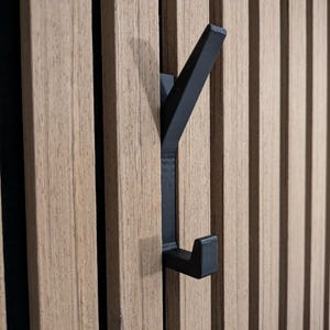 May include: A black metal hook mounted on a wood panel wall. The hook is shaped like a Y with a rounded end.
