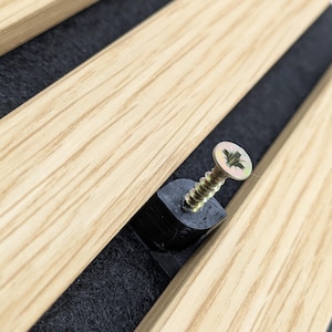 May include: Close-up of wooden slats with a black backing and a gold screw. The wood has a light brown colour with visible grain. The screw is partially inserted into a black plastic piece.