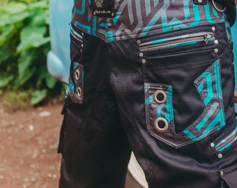 May include: Black cargo shorts with a blue and black geometric pattern. The shorts have multiple pockets and metal eyelets. The waistband has a black belt with a silver buckle that says "DUCKTUS".