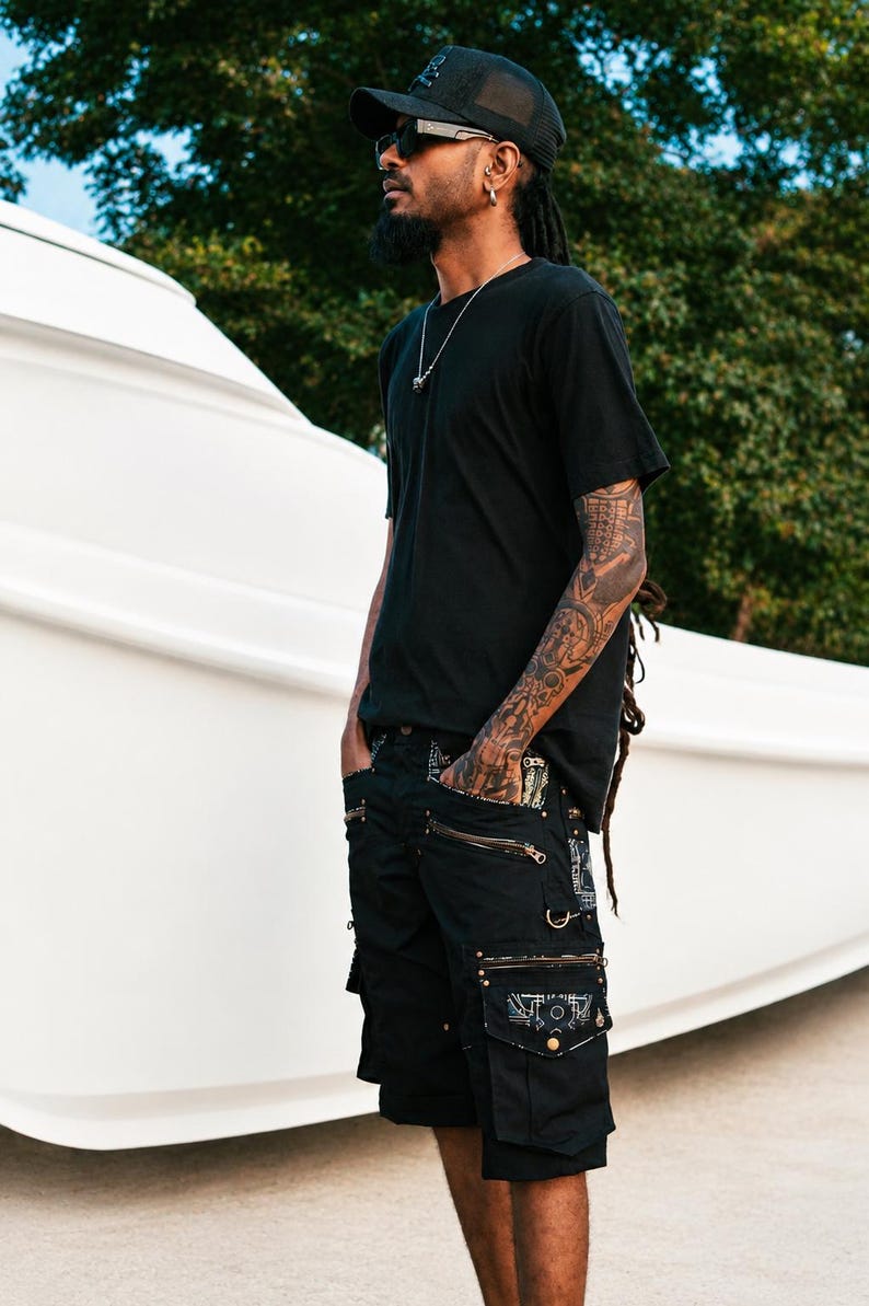 May include: A black t-shirt and black cargo shorts featuring multiple pockets with metallic zippers, decorative metal rings, and patterned fabric accents on the pocket flaps. The shorts have a structured design with visible stitching and hardware details.