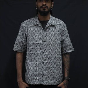 Puede incluir: Un hombre con una camisa de manga corta con estampado blanco y negro y una gorra negra.
