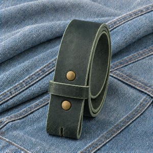 May include: A dark forest green leather belt featuring a smooth matte finish and two circular brass-toned metal rivets securing the strap. The belt is coiled into a loop, showcasing the thick, durable leather construction and the clean edges.