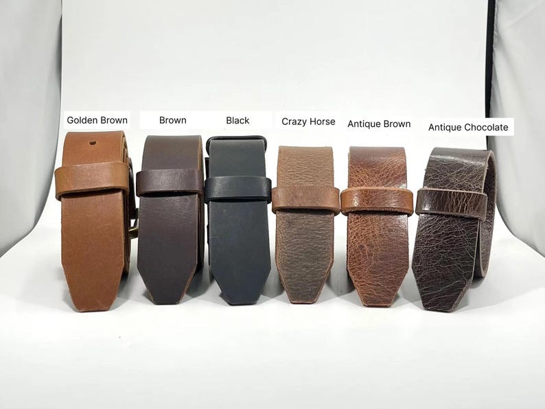 May include: Six leather belts arranged in a row, labeled Golden Brown, Brown, Black, Crazy Horse, Antique Brown, and Antique Chocolate. Each belt features a matching leather keeper loop and a pointed tip, showcasing various shades and textures.