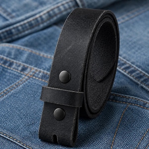 Op de afbeelding: Een opgerolde zwarte leren riem met twee zwarte drukknopen. De riem heeft een gladde, matte afwerking en ligt op een denim achtergrond.