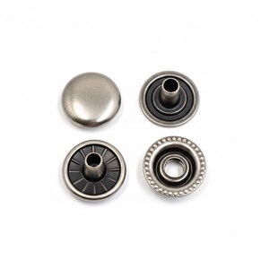 May include: Four antique silver-colored snap fasteners are displayed against a white background. One is a solid cap, and the others are the corresponding parts with varying designs, including a ring of small beads on one.