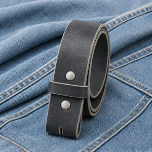 May include: A charcoal gray leather belt featuring a smooth matte finish, a single leather keeper loop, and two circular silver-toned metal rivets securing the strap end. The belt is coiled and displays a thick, sturdy construction throughout.