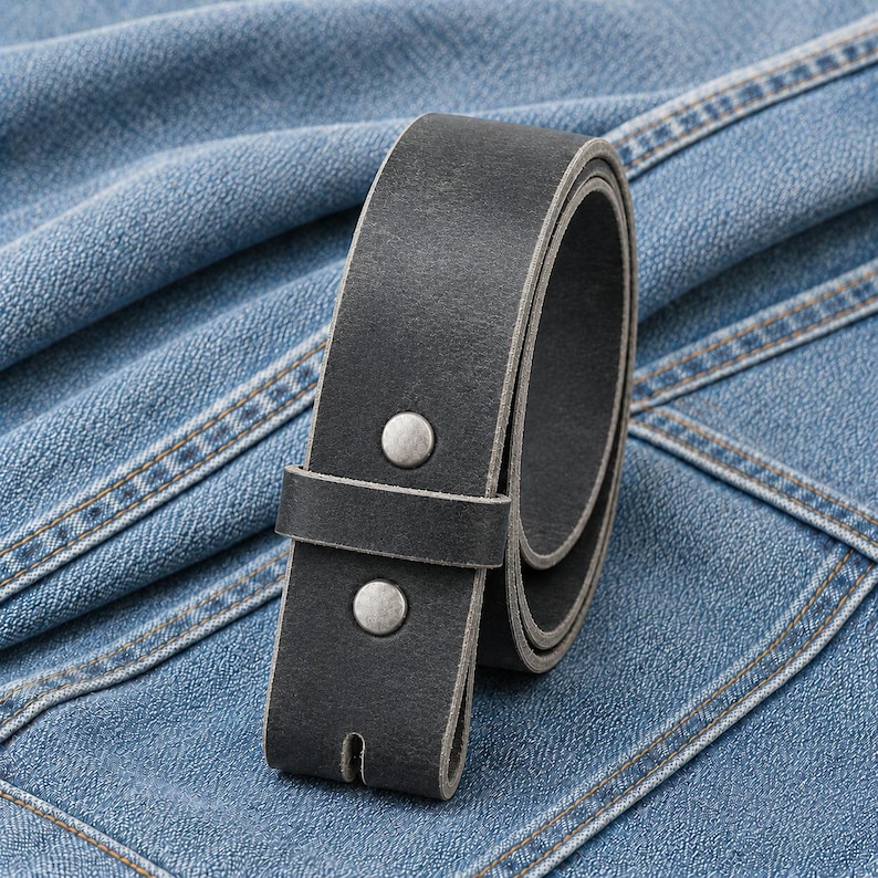 May include: A charcoal gray leather belt featuring a smooth matte finish, a single leather keeper loop, and two circular silver-toned metal rivets securing the strap end. The belt is coiled and displays a thick, sturdy construction throughout.