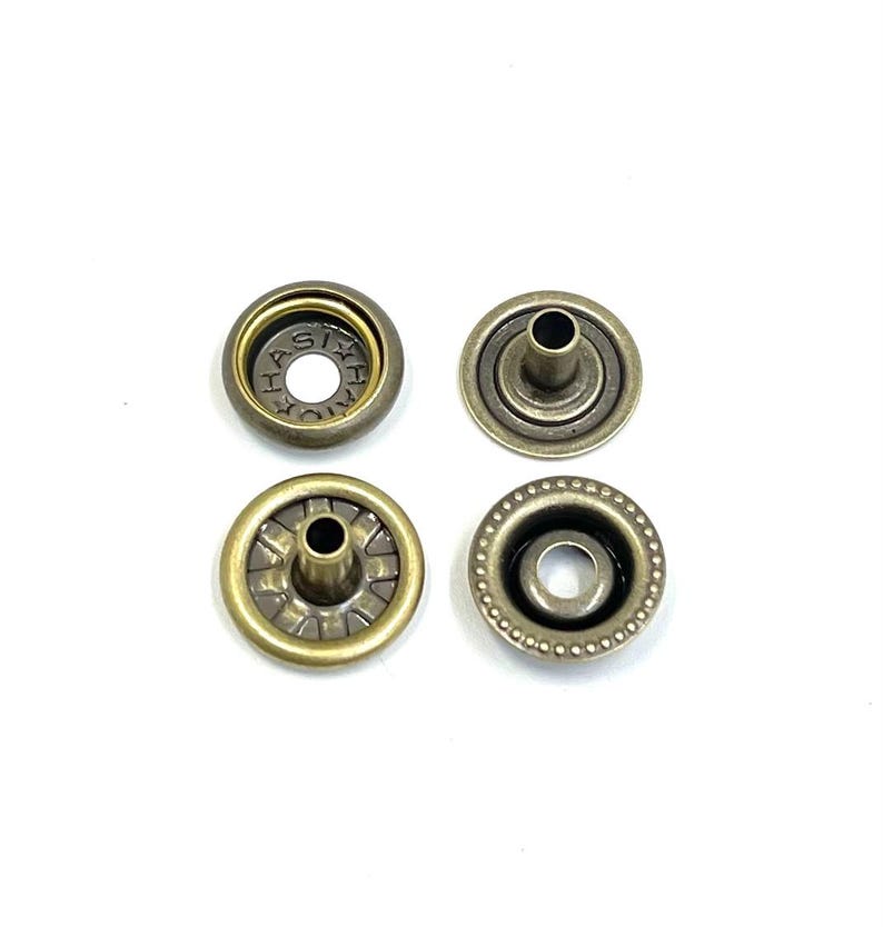 May include: Four antique brass snap fasteners arranged on a white background. Two are complete snaps, and two are the separate pieces. The snaps have a circular design with a central post and a decorative outer edge.
