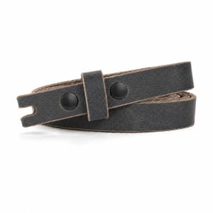 May include: A dark charcoal gray leather strap coiled into a circle. The strap features a matte finish, a single sliding leather keeper, and two black metal snap fasteners. One end of the strap has a notched cutout detail for secure fastening.