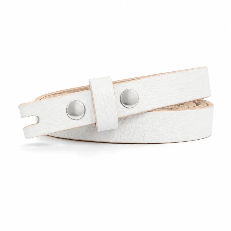 May include: A white leather strap with a textured surface, featuring two polished silver-tone metal snap buttons and a matching sliding leather loop. The strap is coiled in a circular shape, revealing a natural light beige underside.