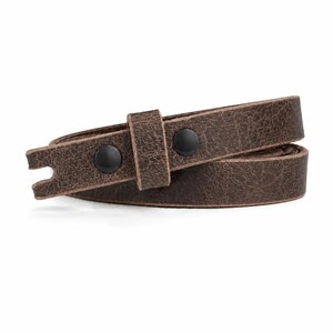 May include: A dark brown leather strap with a distressed, textured finish. The strap features two matte black metal snap buttons and a matching leather keeper loop. The end of the strap is notched with a small cutout, and the material is coiled.