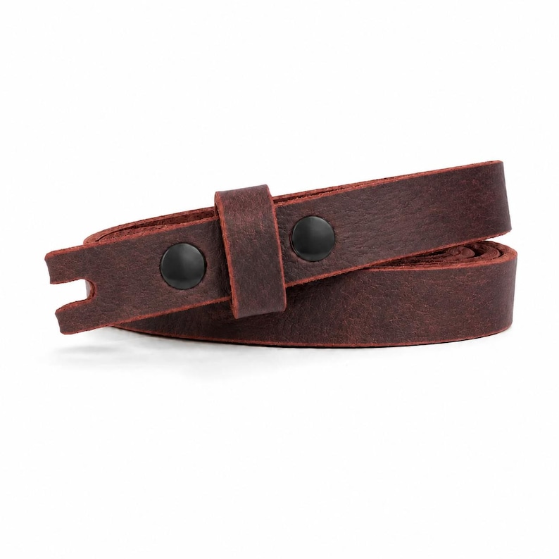 May include: A dark brown leather strap featuring a matte finish and a textured surface. The strap is secured with two black metal snaps and includes a matching leather loop. One end of the strap is cut with a small notch, creating a distinct shape.