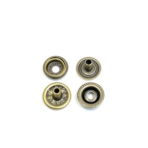 May include: Four antique brass snap fasteners, each with a different design. Two are open-faced with a central hole, and two have a post. The fasteners are arranged against a white background.