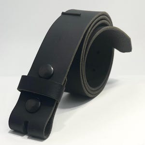 May include: A black leather belt coiled into a circular shape. The belt features a smooth matte finish, a single leather keeper loop, and two black metal snap fasteners located near the end of the strap to secure the closure mechanism.
