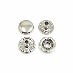 May include: Four silver-colored snap fasteners are displayed against a white background. The set includes two male and two female components. The top piece is a smooth, rounded cap. The other pieces have a central post and a circular design.