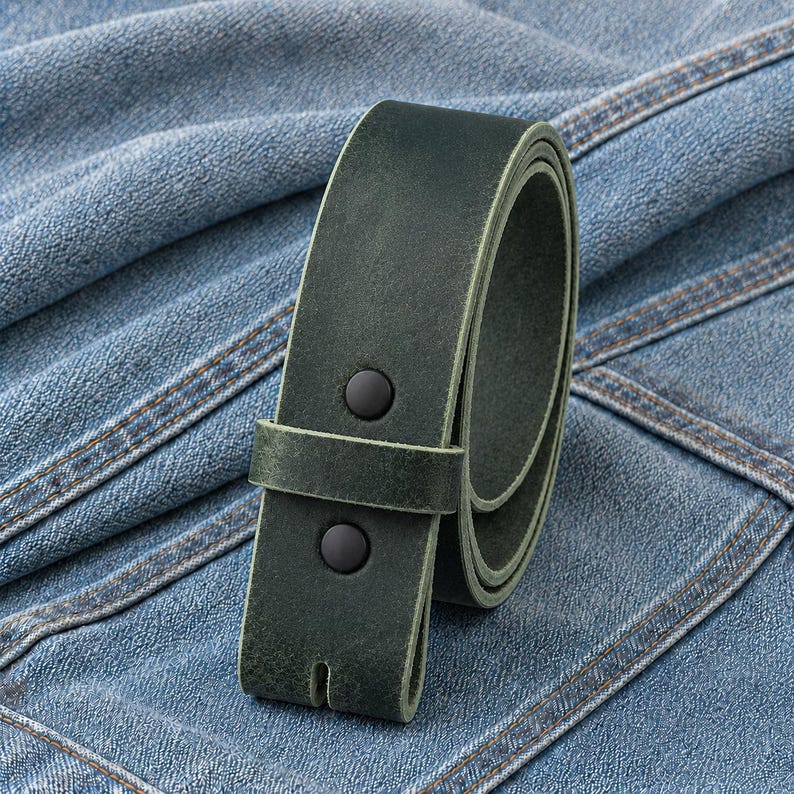 May include: A rolled-up, dark green leather belt with two black button studs. The belt is set against a backdrop of blue denim fabric.