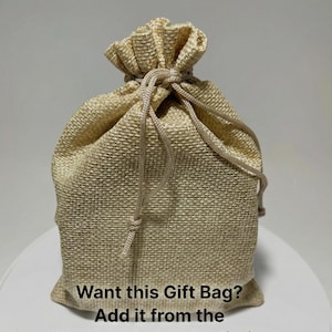 Op de afbeelding: Een beige jute cadeauzak met een trekkoordsluiting. De zak is aan de bovenkant vastgebonden en heeft de tekst "Want this Gift Bag? Add it from the 'Custom Upgrades' listing!" op de voorkant.