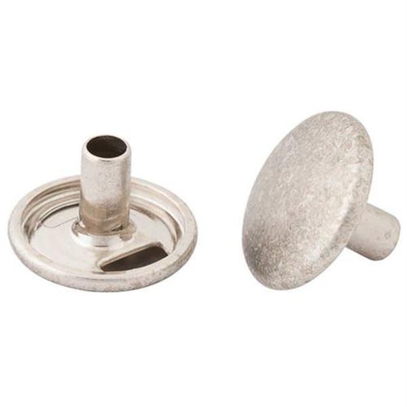 May include: Two silver-colored snap fasteners. One is a circular base with a central tube and a slot. The other is a rounded, button-like piece with a small post. These fasteners are commonly used in clothing and accessories.