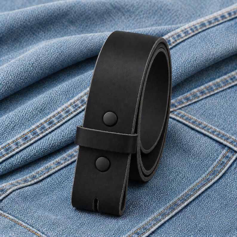 May include: A rolled-up black leather belt with two black snap closures. The belt is shown against a blue denim background. The belt is a classic accessory.