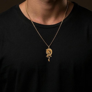 May include: A gold dragon pendant necklace. The pendant, with detailed craftsmanship, hangs from a fine chain. The necklace is shown against a dark backdrop.