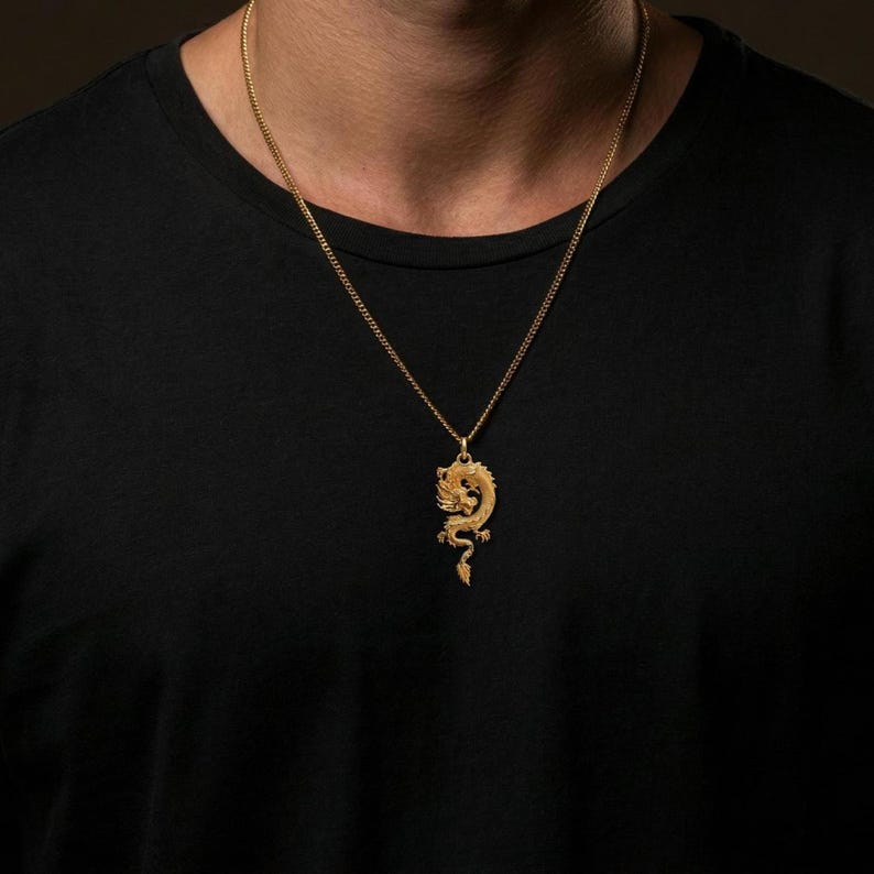 May include: A gold dragon pendant necklace. The pendant, with detailed craftsmanship, hangs from a fine chain. The necklace is shown against a dark backdrop.