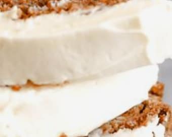 May include: Close-up of a layered carrot cake with a thick layer of white frosting. The cake is made with shredded carrots and spices, and the frosting is smooth and creamy.