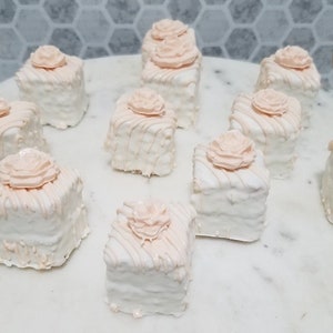 Op de afbeelding: Een schaal met negen witte en roze mini-taartjes, elk met een enkele roze roos erop.