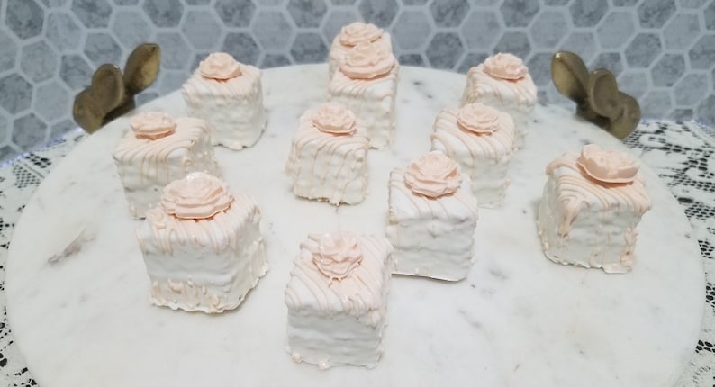 Op de afbeelding: Een schaal met negen witte en roze mini-taartjes, elk met een enkele roze roos erop.