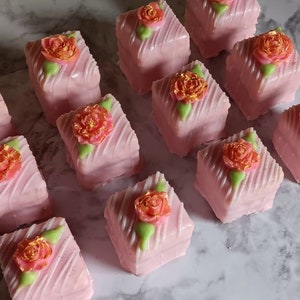 Op de afbeelding: Een verzameling roze en witte petit fours met gouden en groene bloemdecoraties.