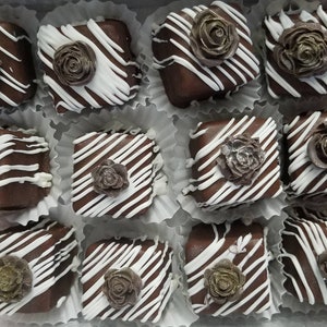Op de afbeelding: Een verzameling van twaalf chocoladevierkanten versierd met witte chocoladestralen en een bruine suikerroos erop.