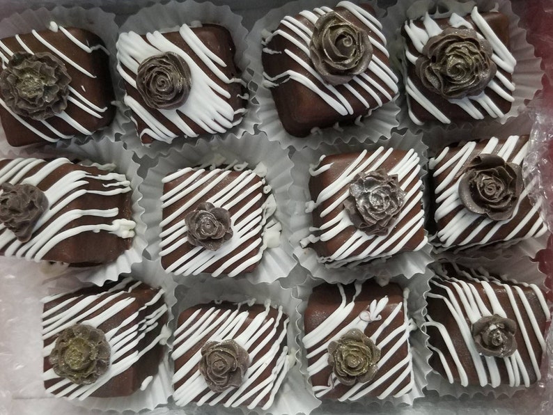 Op de afbeelding: Een verzameling van twaalf chocoladevierkanten versierd met witte chocoladestralen en een bruine suikerroos erop.