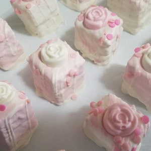 Op de afbeelding: Een verzameling roze en witte vierkante taarten versierd met witte rozen en roze sprinkles.