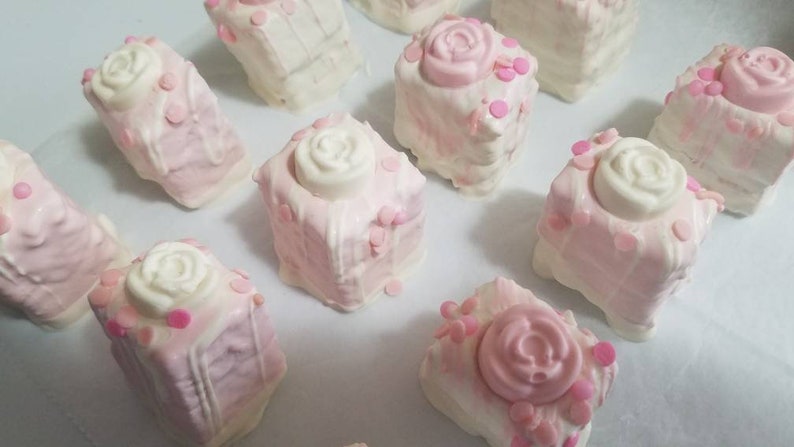 Op de afbeelding: Een verzameling roze en witte vierkante taarten versierd met witte rozen en roze sprinkles.