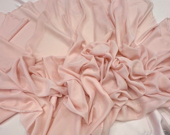May include: A pale pink sheer fabric with a soft, flowing texture. The fabric is draped and folded, creating a delicate and airy look.