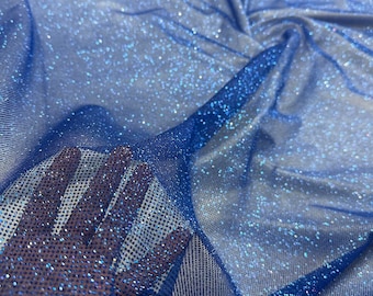 May include: Close-up of a vibrant blue fabric with a shimmering, glittery texture. The material appears to be a sheer mesh, with a hand visible through the fabric. The fabric is gathered and draped, creating folds and shadows.