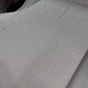 May include: A roll of white fabric with a dense pattern of small, sparkling embellishments. The fabric has a fine mesh backing, and the surface is covered in tiny, reflective elements, creating a shimmering effect. The fabric is suitable for apparel and craft projects.